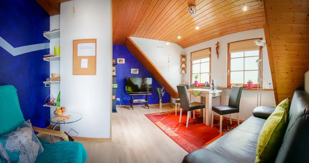 Wohnzimmer mit Couch, Esstisch und Fernseher unter Holzdecke